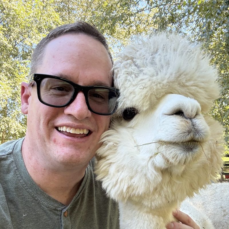 Mickey Mellen outdoors, cheek to cheek with a white alpaca